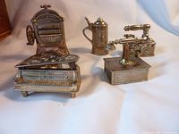 Front view of five metal miniatures displayed on white cloth, showing grand piano, iron, stein, telephone and wringer