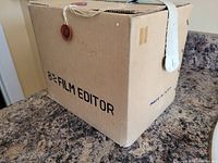 Original cardboard box labeled '8mm Film Editor' placed on a countertop with a fabric background visible.