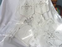 White linens with intricate floral embroidery and lace trim laid out showing details of borders and patterns