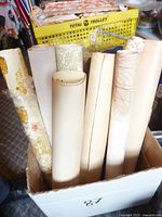 Box showing 7 wallpaper rolls, including floral and textured designs, some unsealed.