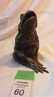 Front angle view of handcrafted bronze frog sculpture showing open mouth and raised hand.