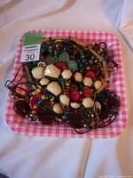 Overhead photo of a colorful assorted lot of jewelry pieces including bead necklaces, wooden bangles, and various pendants on a pink checkered tray.