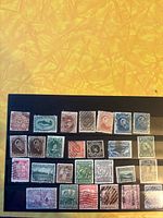 Photo of various used early Newfoundland postage stamps displayed on black album sheet with yellow background.