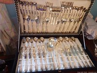 Photo of the full open box showing entire set including forks, spoons, knives, and serving pieces arranged in elastic slots inside original box with houndstooth-patterned edge.