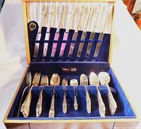 Full view of the 45-piece silverware set neatly arranged inside a wooden chest lined with blue velvet.