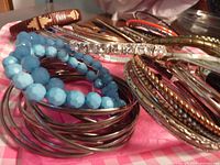 Close-up of assortment of bracelets showing blue beaded, metal bangles, and rhinestone bracelet on a pink cloth.