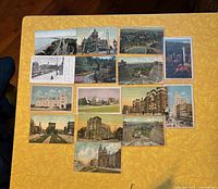 Photo of 17 Hamilton postcards laid out on yellow patterned tablecloth featuring various historic buildings, bridges, and cityscapes.
