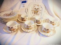 Overview of the set arranged showing multiple cups on saucers, stacked plates, and the square serving tray at back