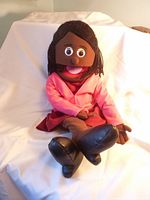 Full view of the hand puppet seated with legs crossed, showing face, hair, and outfit.