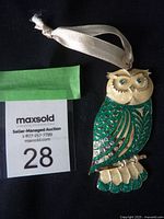 Full view of a peacock blue owl ornament with gold-tone metal, blue Swarovski crystals on wing detail, cream-colored face, and attached satin ribbon for hanging.