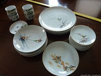 Photo displaying a variety of hand-painted Japanese plates and tea cups with floral and bird patterns.
