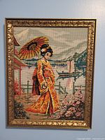 Full view of the framed needlepoint artwork showing a Japanese woman holding a parasol by a scenic lakeside with surrounding nature and architecture.