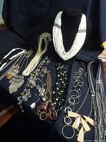 Wide shot of all statement necklaces arranged on a black surface and display bust revealing variety in material and style.