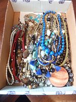 Box lot of various necklaces tangled together showing different colors, bead styles, pendants, and chains.
