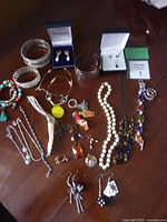 Photo showing a broad assortment of jewelry items on a wooden surface, including bracelets, necklaces, earrings, and pendants in various materials and colors.