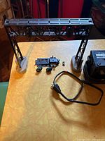 View of the Lionel electric train signal bridge with signal mechanism and transformer with power cord on a table.