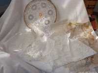 Photo of round lace doily with colorful crochet flowers and white lace-trimmed fabric pieces.