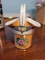 Front view of Noritake hand painted china basket showing yellow/gold background and floral designs.
