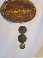 Brown leather pouch embossed with a beaver in a pond and the word 'AMISK' alongside three coins of varying sizes below it.