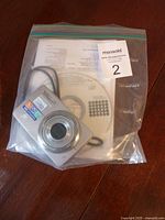 Olympus digital camera, instruction booklet, and software CD in ziplock bag on wood surface