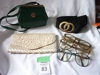 Green musical purse, black fabric belt with metal buckle, white beaded clutch, and three pairs of vintage glasses shown on white background.