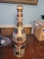 Front view of solid brass decorative bottle holder with peacock design on wooden table.