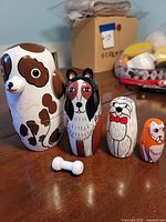 Four hand-painted wooden nesting dog dolls from largest to smallest with a white bone accessory in front. Original box and surrounding background visible.