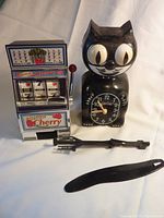 Toy slot machine and cat clock shown together, slot machine has lever and colorful cherry graphics, cat clock is black with large eyes.