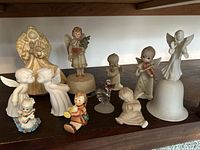 Wide shot of 10 assorted angel figurines of various sizes and makers including Schmid music box and porcelain angels.
