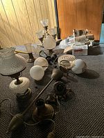 Photo showing assorted antique and vintage light fixtures including hobnail glass lamp, chandelier, globes, and other lighting components on carpeted floor.