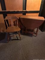 Photo showing wooden antique gate leg drop leaf table next to wooden chair. Table legs are folded down with leaves closed.