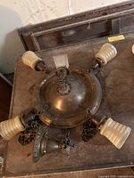 Top view of circular ornate metal light fixture base with four attached ribbed glass lanterns, heavy chains for suspension visible.