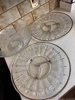 Two clear glass trays with 14 divided sections on countertop next to a footed glass bowl with floral pattern.