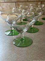 Set of 11 vintage cocktail glasses with green bases and stems arranged on countertop.