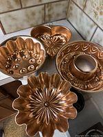 Four copper gelatin molds displayed on a counter showing distinct shapes and patterns