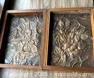Two framed copper relief art pieces with floral designs shown side by side on wood surface.