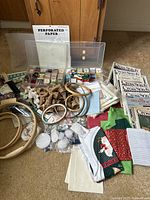 Wide view showing whole collection of cross stitch, embroidery, and sewing supplies including hoops, fabrics, baskets, books, and perforated paper.