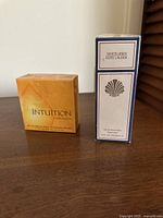 Photo of two sealed boxed Estée Lauder perfumes: Intuition and White Linen sitting side by side on wooden surface.