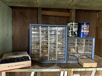 Two blue plastic multi-drawer organizers filled with various small hardware pieces and fasteners. One open box of loose nails placed in front. Two metal paint cans behind the organizers.