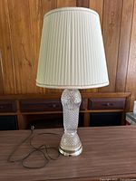 Full view of the glass and brass table lamp with white pleated shade.