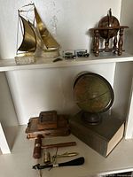 Overall lot on shelves showing brass sailboats, Model T cars, globes, wooden box, gavels, arrowheads, and dictionary.