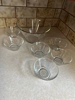One photo showing the large salad bowl surrounded by six smaller bowls, all glass with hobnail bottoms, placed on kitchen countertop.