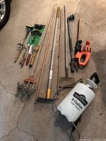 Photo showing a variety of garden tools including rakes, a garden weasel, an orange electric hedge trimmer, and a white Groundwork 2-gallon sprayer.