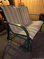 View of the Lawn Glider Loveseat showing the front and side profile with woven striped seat and green metal frame.