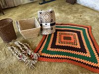 Photo of the two macrame plant hangers, granny square blanket, Berkshire quilted throw, and two baskets displayed on a carpeted floor.