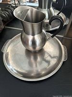 Stainless steel pitcher placed on a round serving tray showing full set