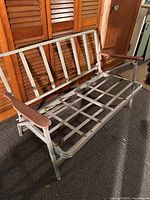 Midcentury aluminum patio sofa showing the front with wooden armrests and metal grid seat and back support.