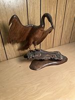 Left side view of wood bird sculpture on natural wood base showing carved details and wood grain.