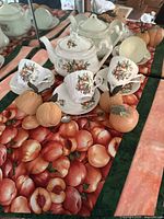 Photo of tea set with teapot, teacups and saucers arranged on the peach themed quilted table runner with realistic peach fruit images.