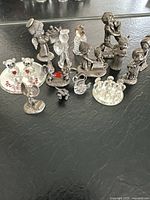 Photo showing overall pewter and crystal miniature collection including angels, mice, bears, children figures, and small animals on black surface with pen for size.